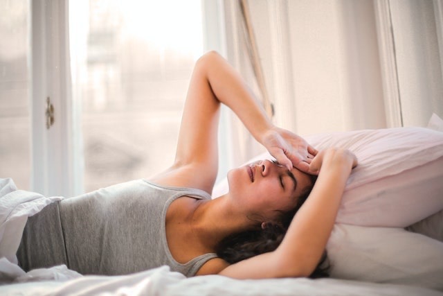 Mujer en la cama con dolor de migrañas almohada cervical Brezzz
